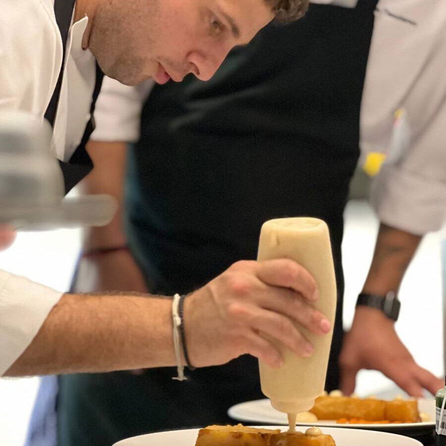 A chef’s hands preparing a gourmet dish on a plate.